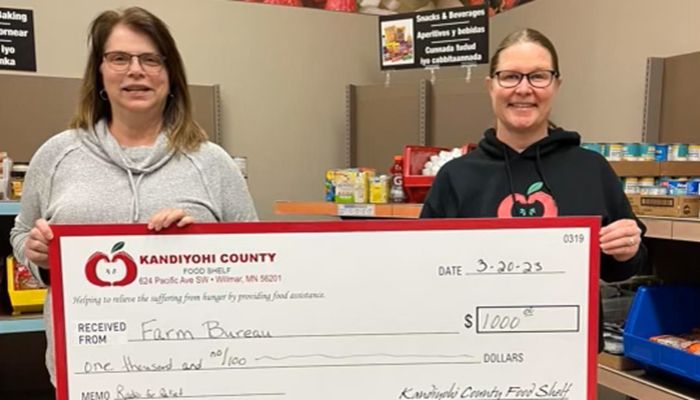 two women standing together holding large donation check