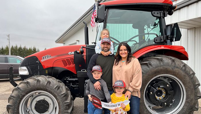 Two adults and three children standing in front of a tractor