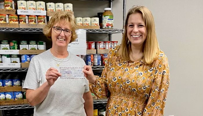 two women standing together holding large donation check