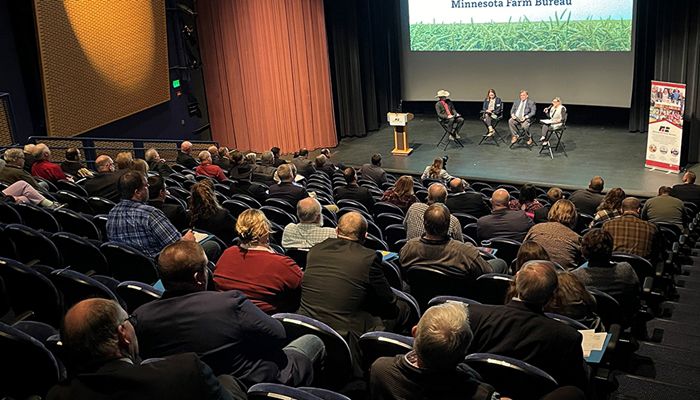 photo of large group of people sitting in an auditorium listening to a panel of speakers on a stage