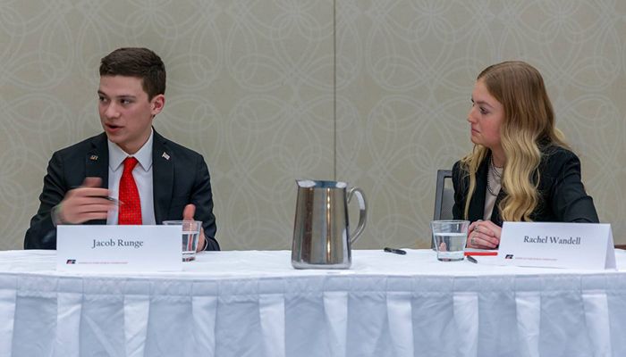 Jacob Runge talking in a competition, seated at a table next to another person
