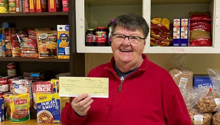 woman standing in front of food shelves holding a check