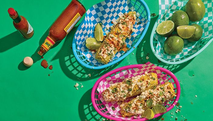 overhead photo of Mexican street corn, hot sauce bottles and limes