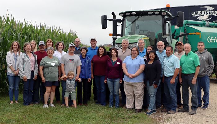 large group of people standing in front of a tractor and corn field
