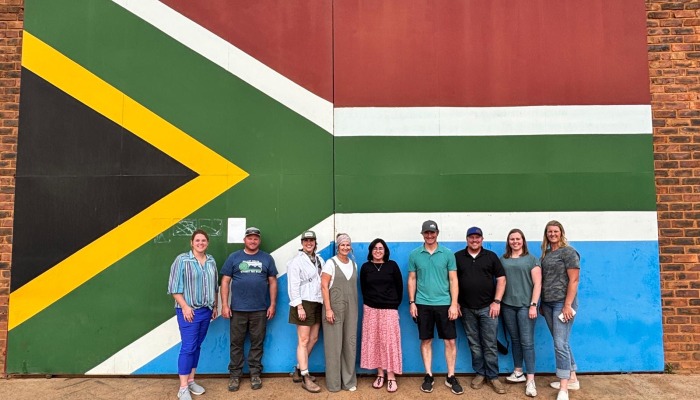 group of people standing in front of a mural with the flag of South Africa