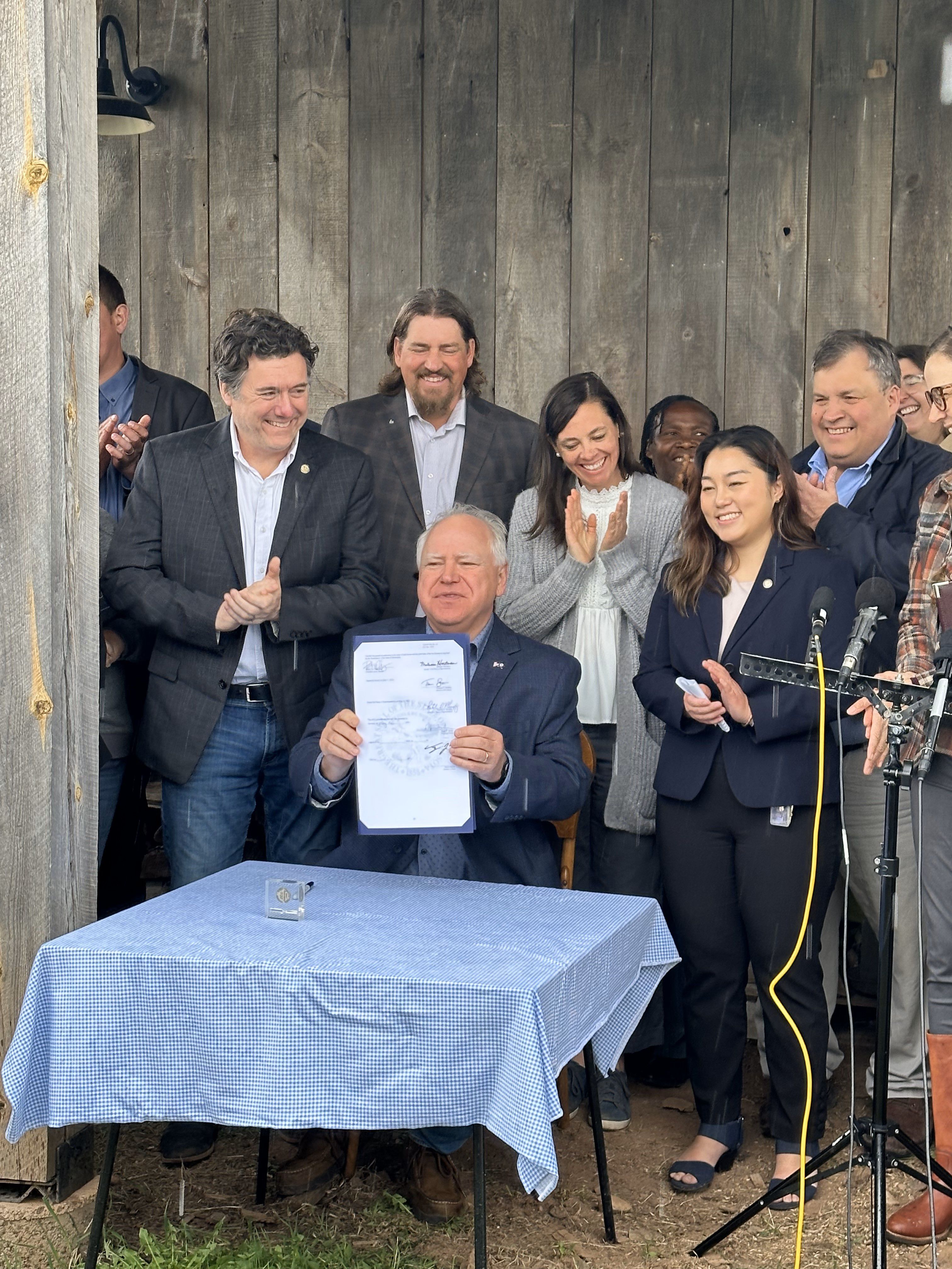 group of people standing behind a man seated at a table holding a piece of paper